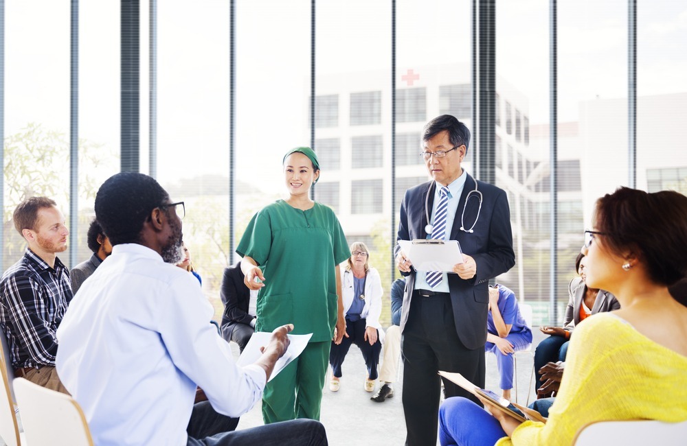 A diverse group of people sits in a circle listening to a doctor and nurse practitioner address important health issues.