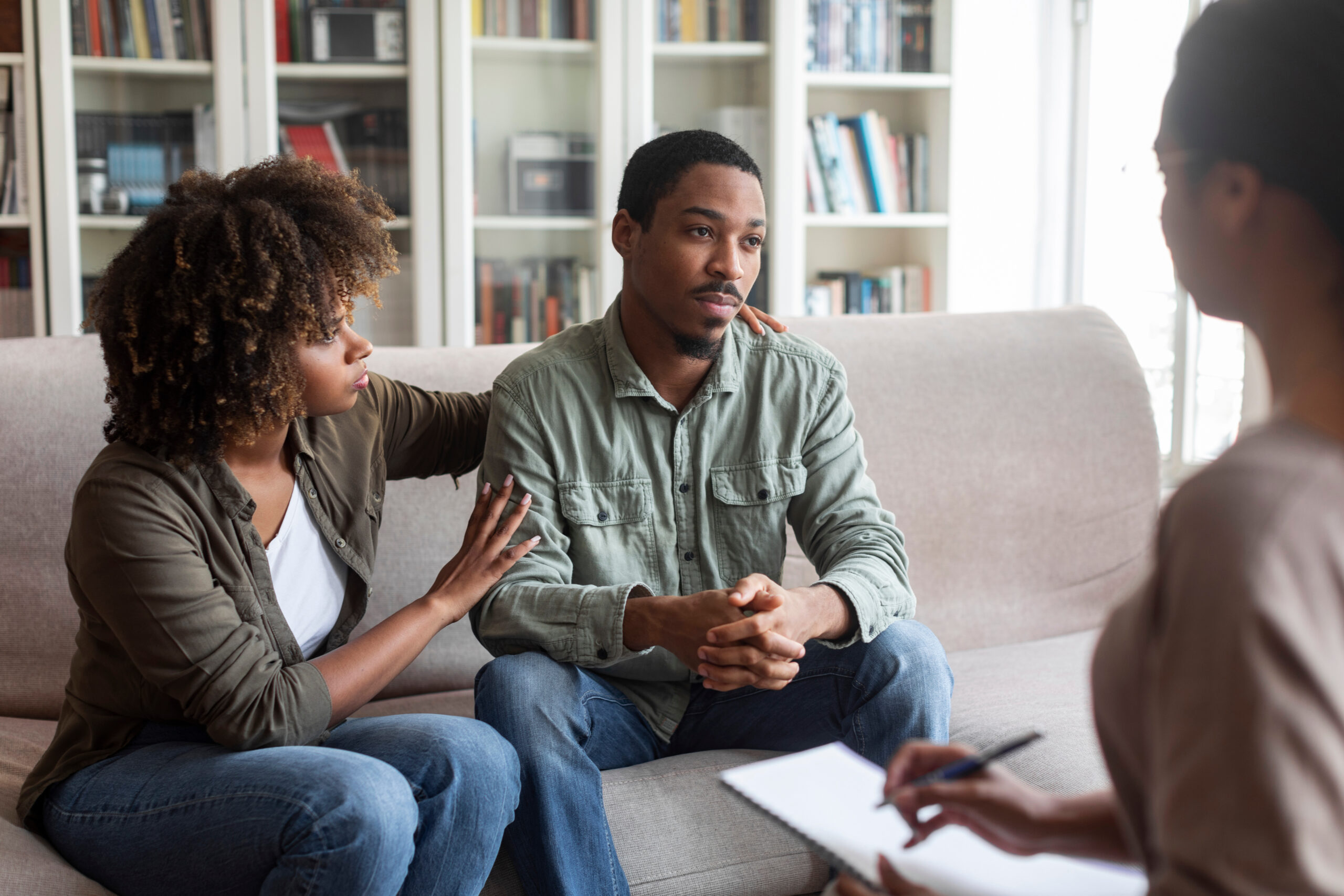 Loving black woman embracing her depressed husband, therapy session