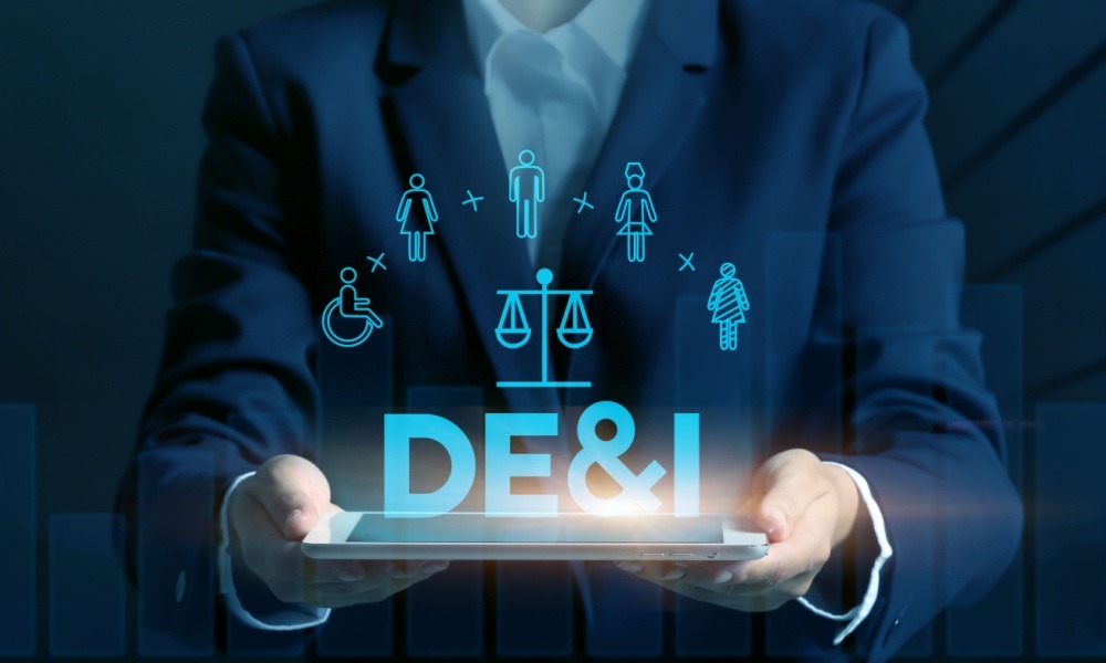 Conceptual image of a businesswoman holding a tablet PC superimposed with a virtual screen with the phrase “DE&I” on a dark background.