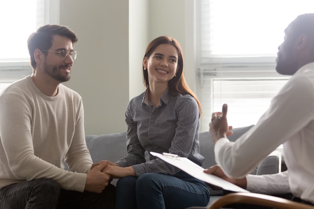 A happy couple hold hands while speaking with a marriage and family therapist