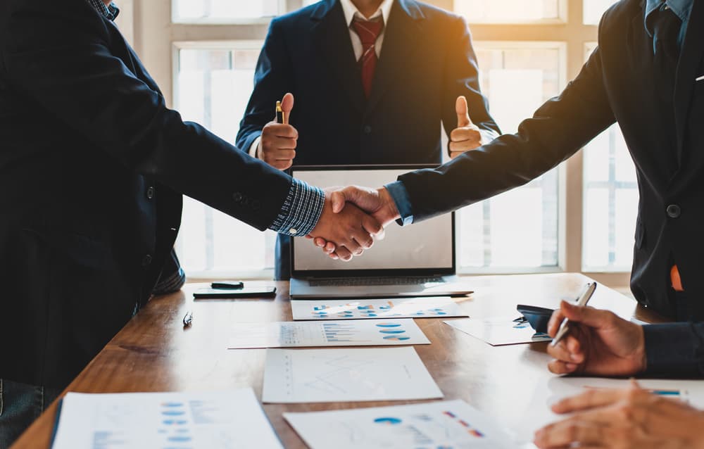 A business arbitrator gives a thumbs up as two businessmen shake hands over a negotiated settlement.