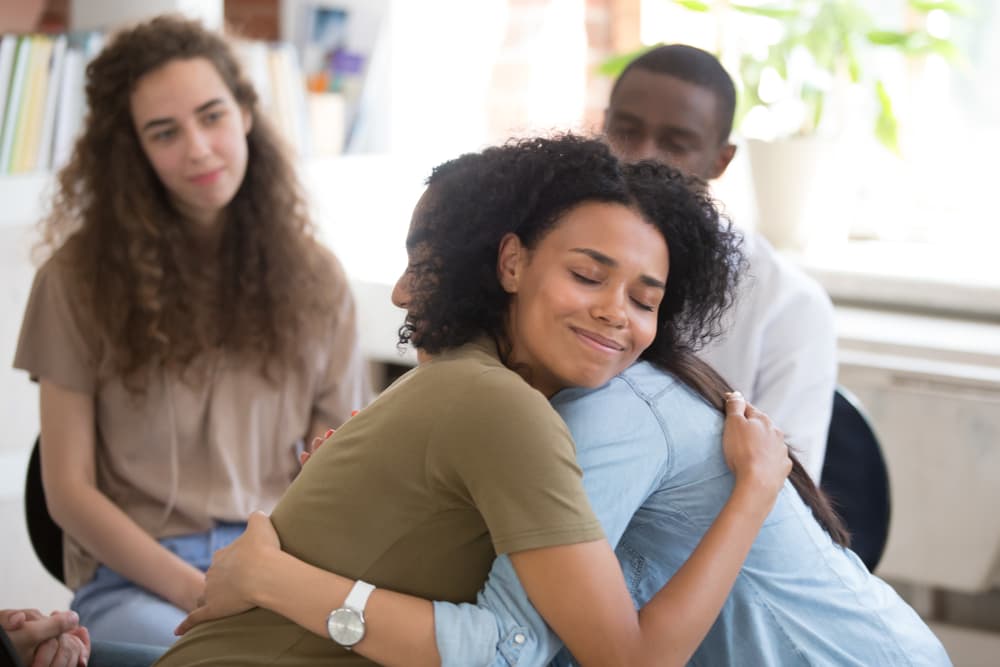 An addiction counselor hugs a client in recovery during a group therapy session