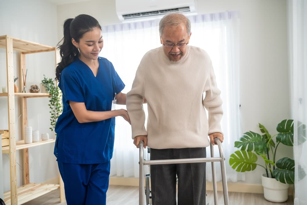 A caregiver assists an elderly gentleman with physical therapy.
