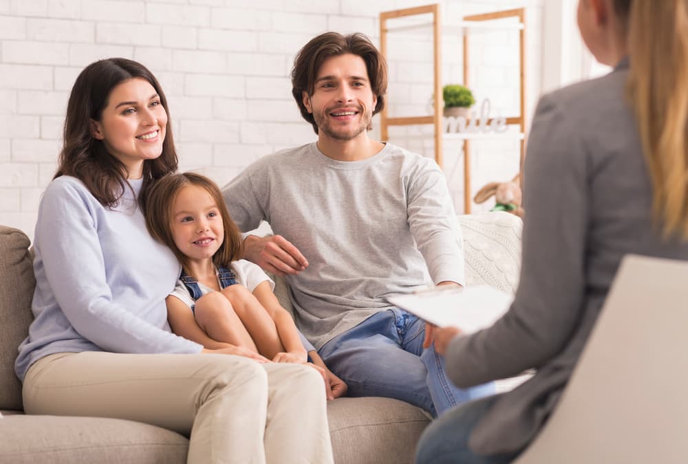 A happy young family sits on a couch during a family therapy counseling session.