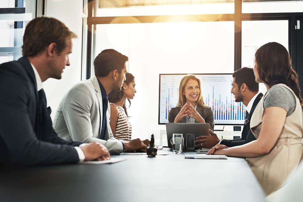 A businesswoman sits at the head of a conference table leading a meeting.