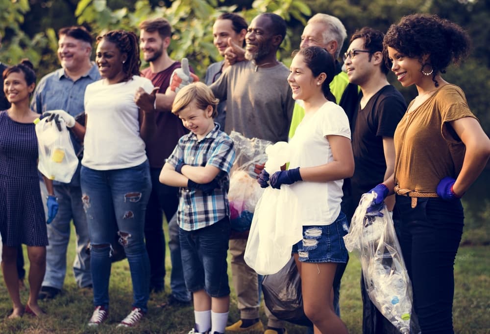 A friendly-looking, diverse group of people smiles for a photograph after a community park clean-up.