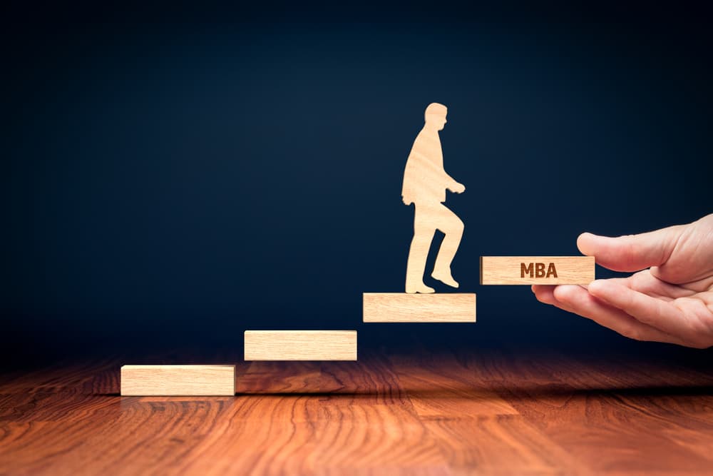 A conceptual image of a miniature model of a step and a man climbing to the top step labeled “MBA.”