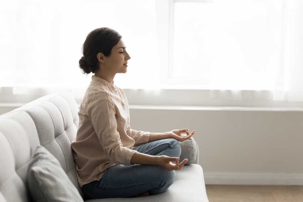 A woman meditates while sitting on a couch.