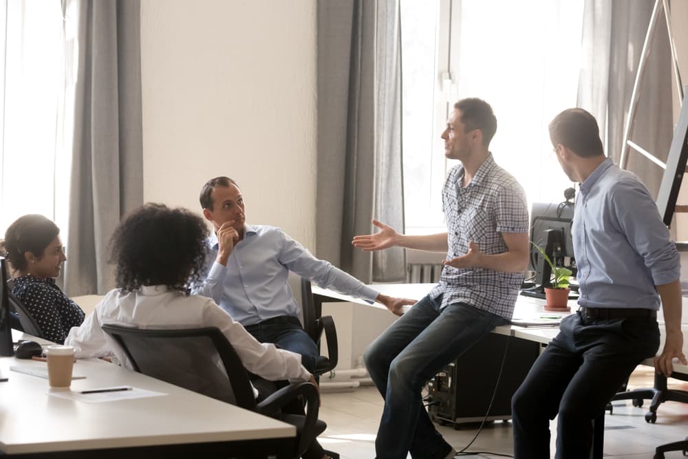 A workplace counselor meets informally with a diverse group of employees in a modern office meeting room.