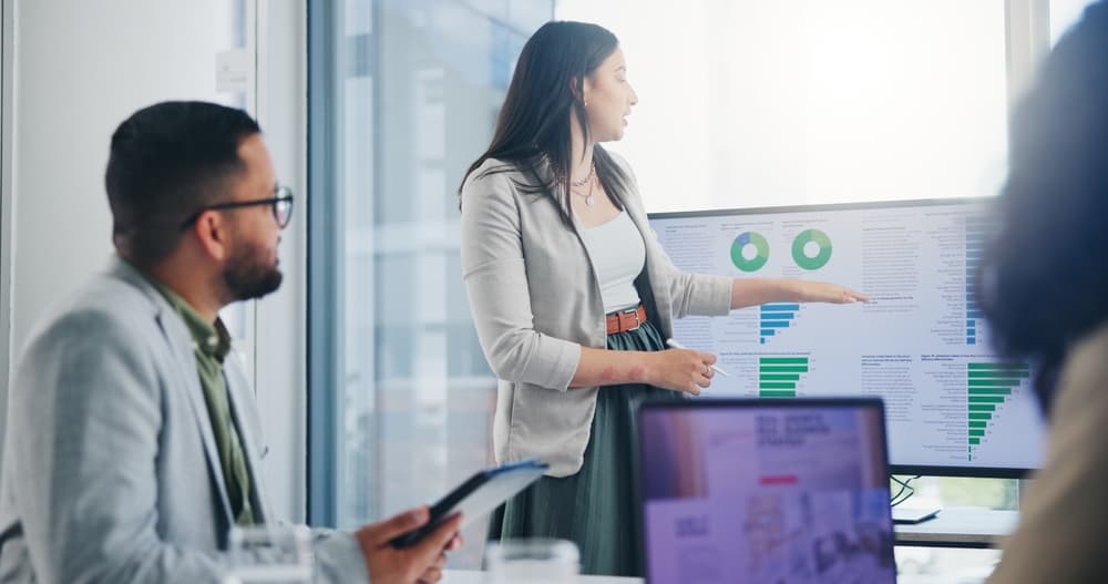 A business analyst presents online data to her team in a modern business meeting room.