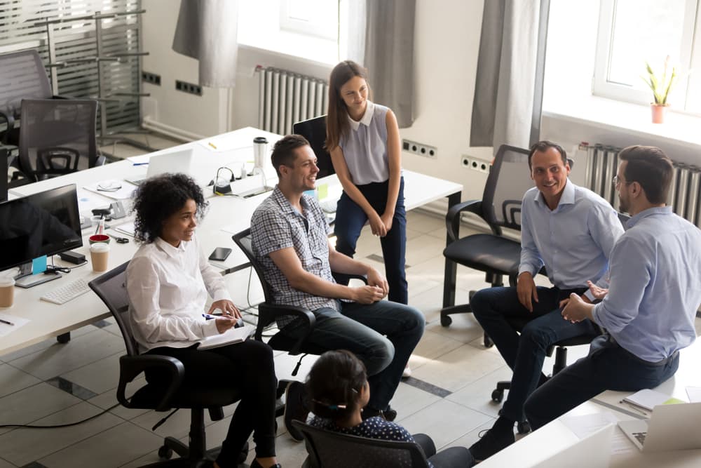 A diverse, collegial group of employees holds an informal meeting in a modern office environment.