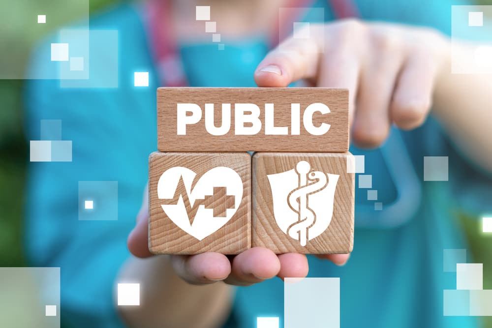 A conceptual image of a close-up of a nurse’s hands holding blocks with the word “public” on top of public health-related icons.
