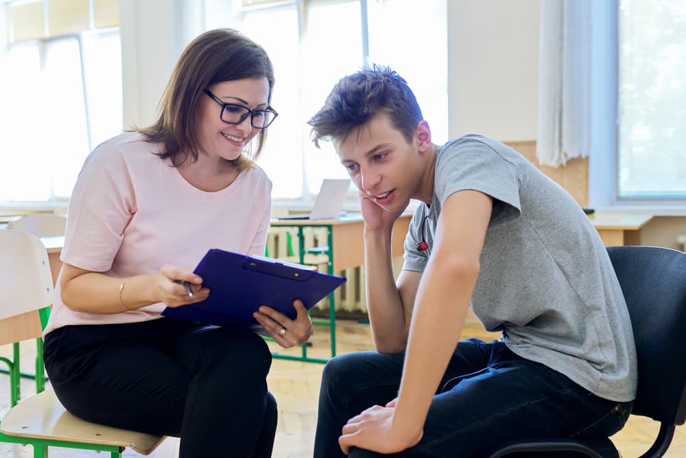 A school social worker holds a clipboard and helps a high school student consider his educational options.