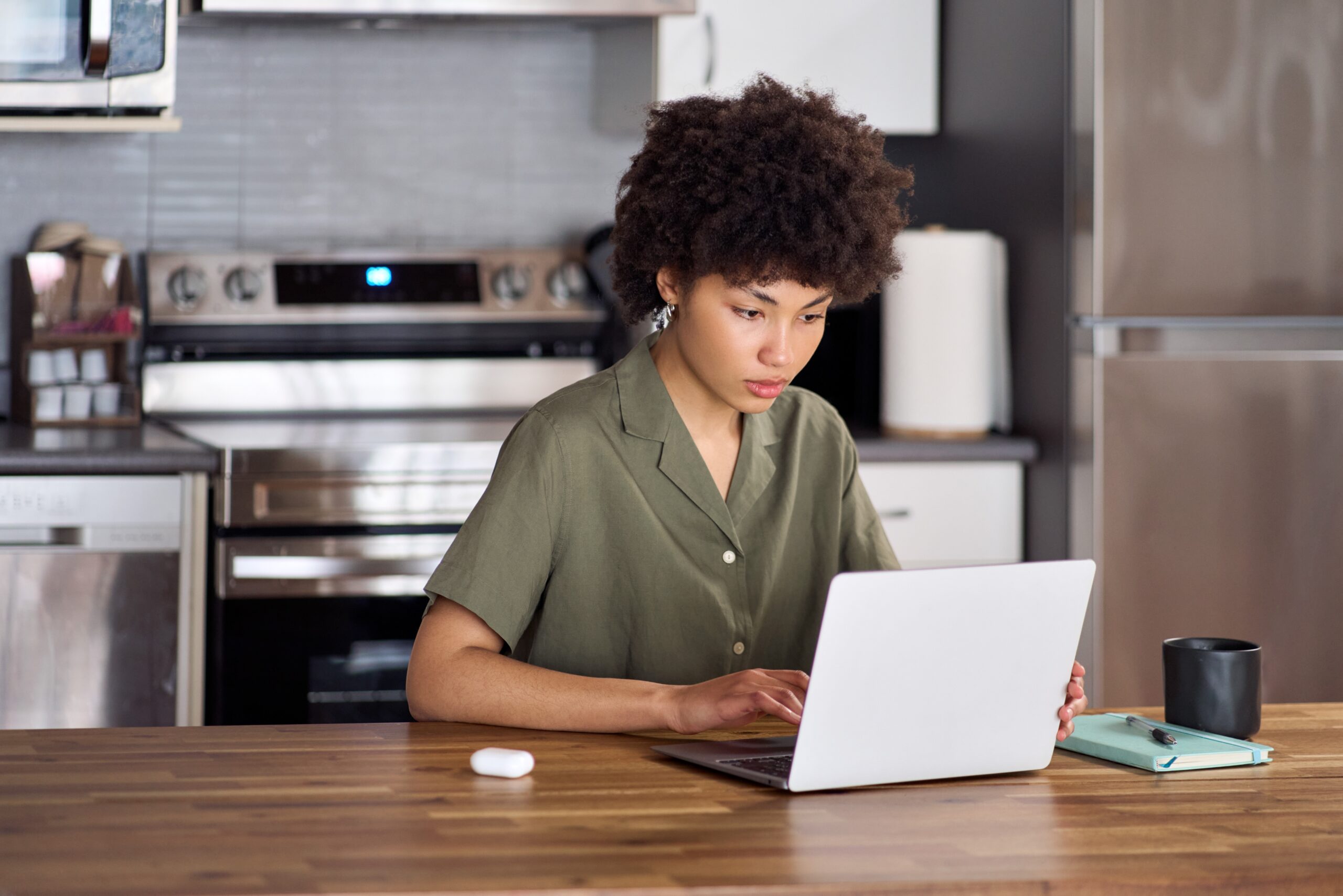 An African American woman sits at her kitchen table studying on her laptop.