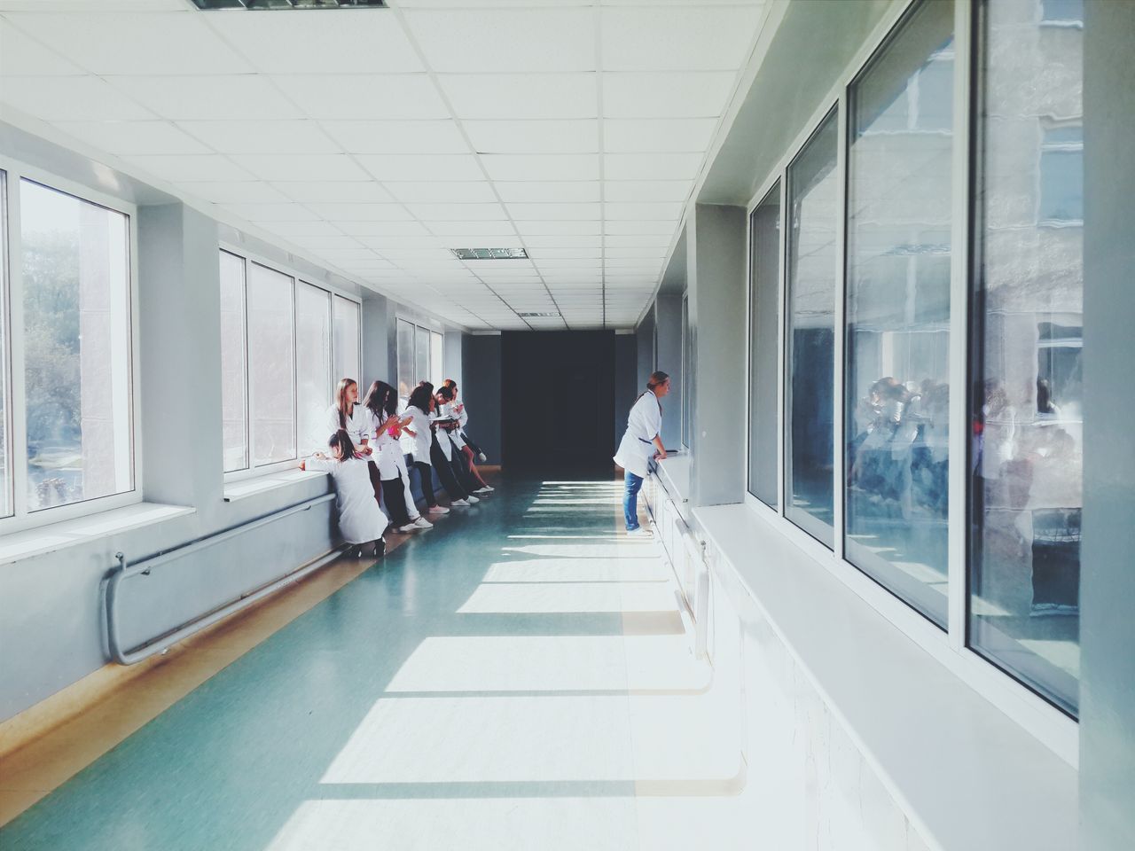 A group of medical students or healthcare staff wearing white lab coats standing in a bright hospital hallway