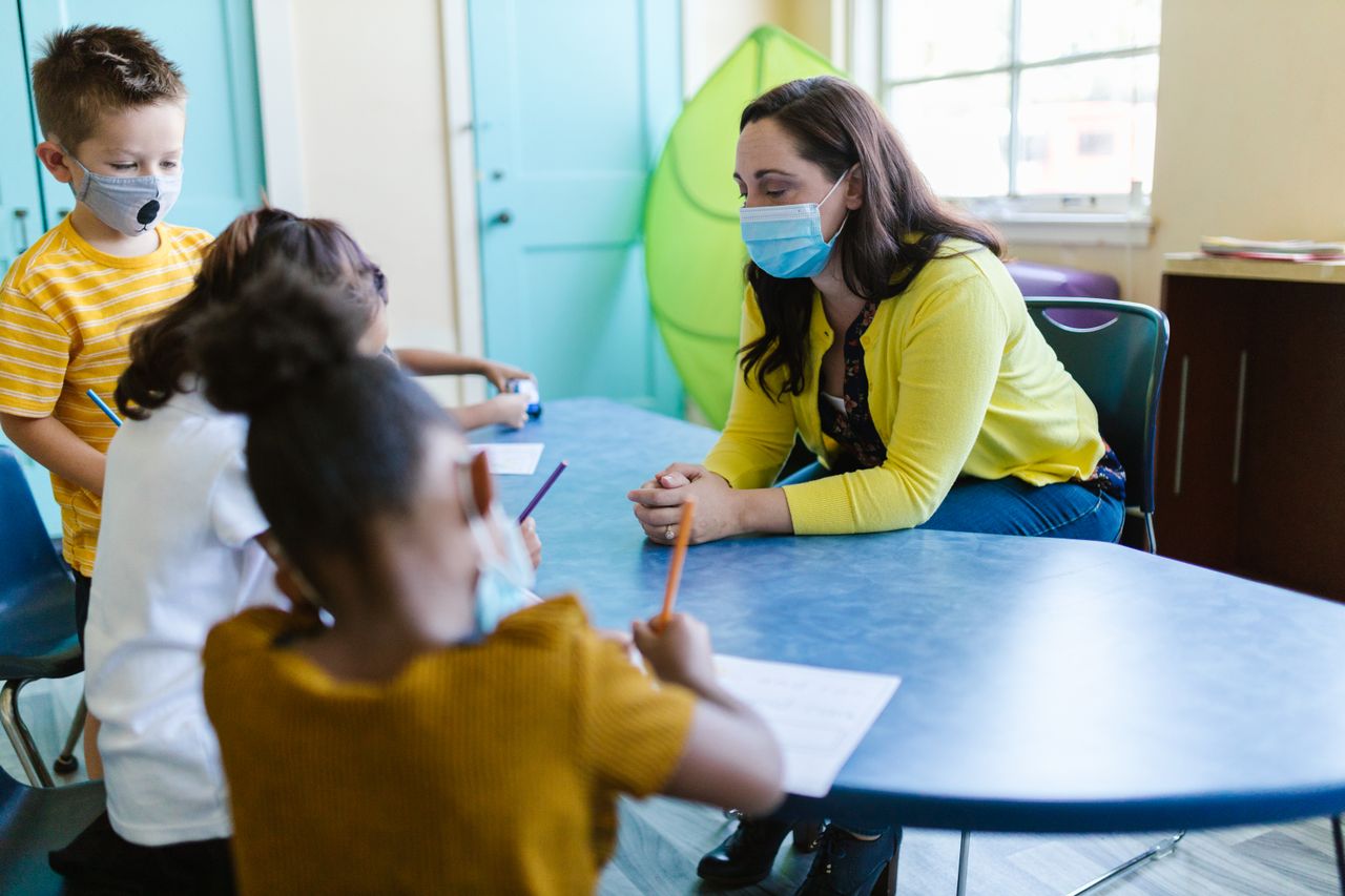 Healthcare educator sitting at a table with three children wearing face masks