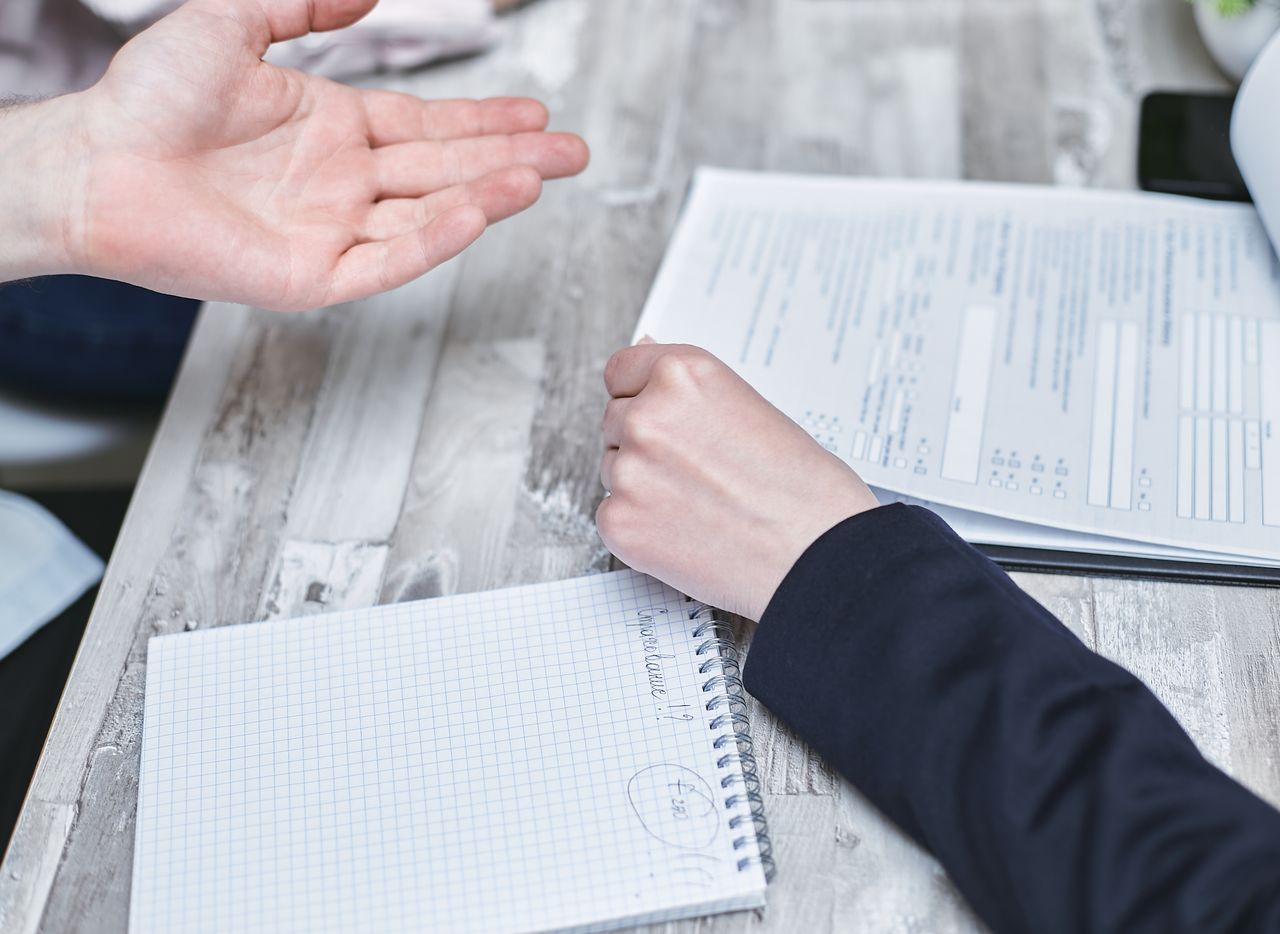 A probation officer in a professional jacket discussing documents and taking notes during a consultation with a client.